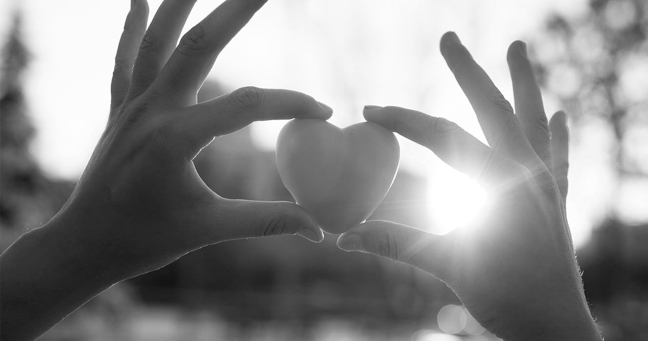 Hands holding heart-shaped stone in sunlight 
